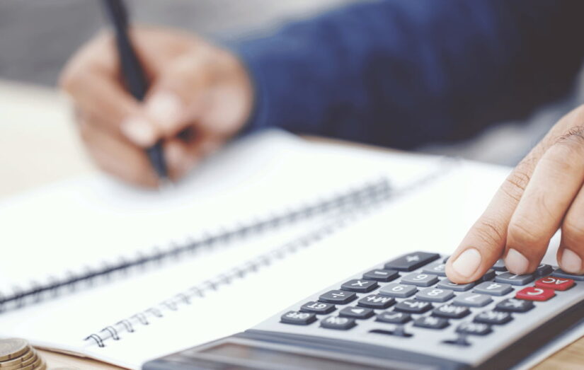 Uma pessoa usando uma calculadora em cima de um notebook.