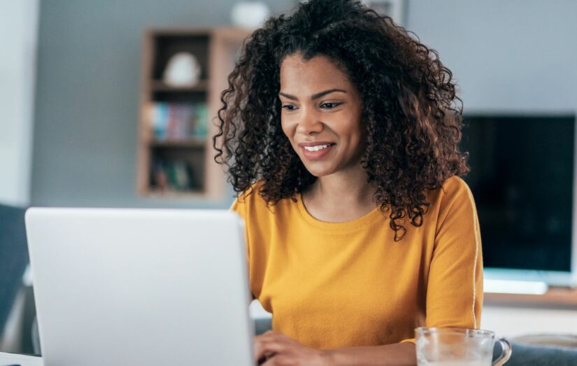 Uma mulher negra com uma camisa amarela trabalhando em home office em seu laptop